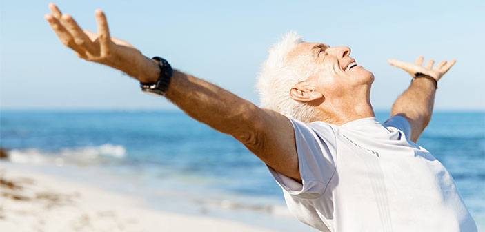 Glad ældre mand ved stranden med udstrakte arme